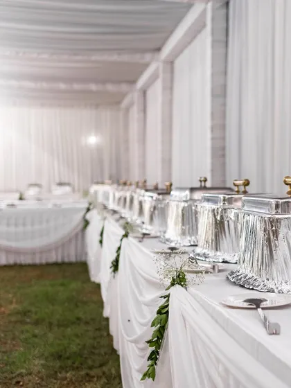 A clean and elegant buffet setup for a reception, draped in white linens with simple green foliage accents. We ensure every aspect of the event, including catering displays, aligns with the overall aesthetic.