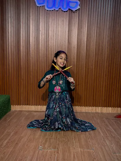 A happy dancer kneels for a photo, showcasing her beautiful printed skirt and dandiya. We make sure every child feels like a star in our studio.