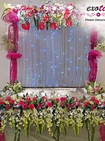 A beautiful puja backdrop with a curtain of fairy lights. The stage is adorned with a mix of pink and white flowers, creating a sparkling and divine effect.