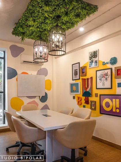 We designed this meeting room with a gallery wall of quirky art and objects, set against a bright yellow circle. The birdcage-style chandeliers and a ceiling covered in artificial greenery add layers of whimsy and creativity.