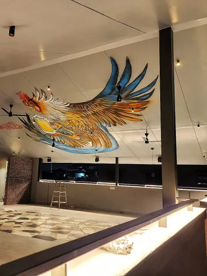A wide shot of the massive rooster mural we painted on the ceiling at Plan B's Kammanahalli location, showing its scale within the large, open space.
