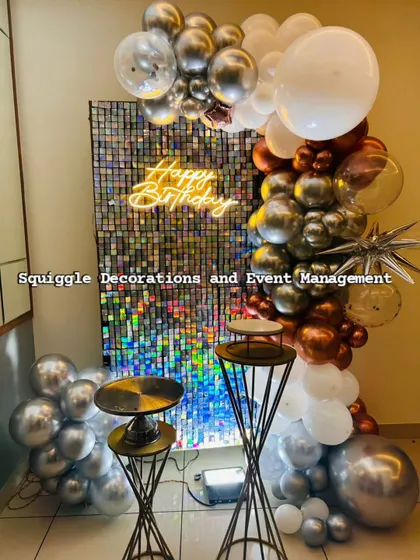 This modern and chic birthday setup features a dazzling holographic shimmer wall that catches the light beautifully. It's complemented by a custom 'Happy Birthday' neon sign and a stylish chrome and copper balloon garland.
