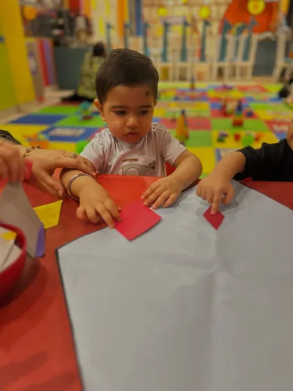 A young child carefully places a shape onto his kite craft, demonstrating concentration and developing fine motor control.
