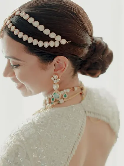 A delicate and serene bridal portrait of Sonali in her white wedding sari, her smile illuminated by soft window light.