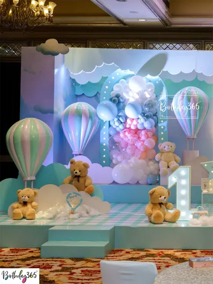 A beautiful stage setup for a hot air balloon and teddy bear first birthday, with soft blue and pastel colors.