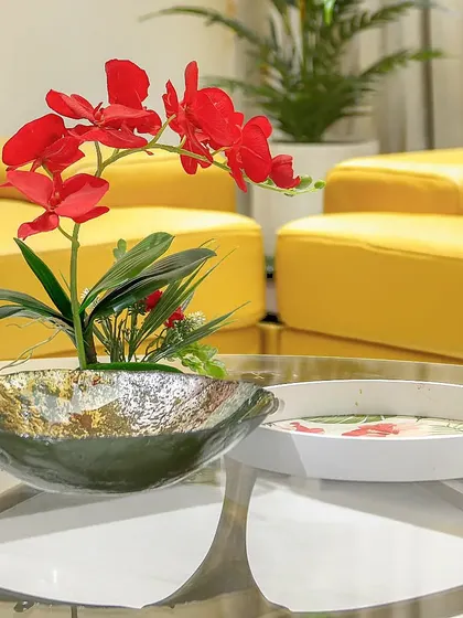 A close-up of a styled coffee table, where vibrant red orchids contrast with a bright yellow sofa.