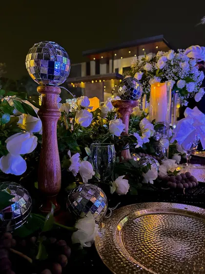 A close up of a table centerpiece from the enchanted forest party. We combined classic white roses with mini disco balls, blending elegance with a fun, retro twist.