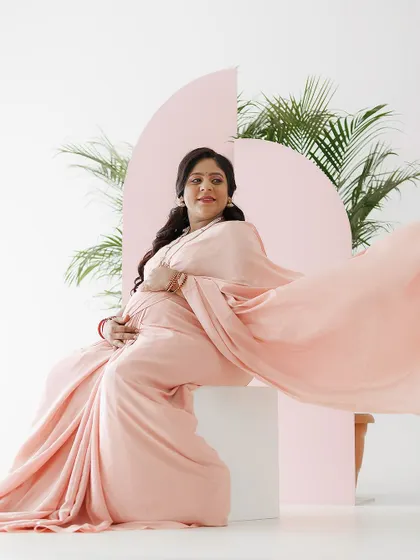 A full-length shot showcasing the elegant drape of the pink saree. The makeup and hair are styled to create a graceful silhouette, perfect for a maternity photoshoot.