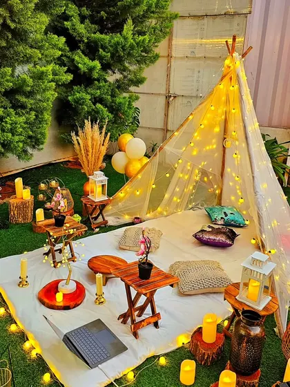 A magical teepee picnic setup for a romantic evening. The tent is illuminated with fairy lights, surrounded by candles and lanterns, creating a dreamy and intimate space.