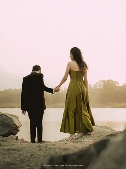 The couple stands at the edge of the water, looking out at the view. This wide shot captures the scale of the landscape and the intimacy of the couple within it.