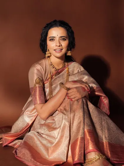 A lovely portrait where the makeup enhances the model's natural beauty. The soft brown background complements the warm tones in the saree and makeup.