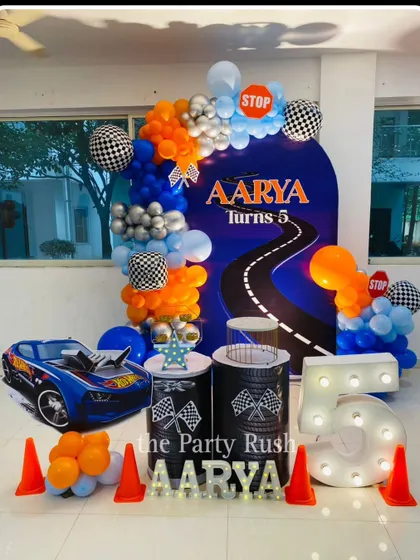 This Hot Wheels theme for Aarya's 5th lap is full of speed and excitement. The decor includes a race track backdrop, a large Hot Wheels car prop, traffic cones, and a big marquee number '5'.