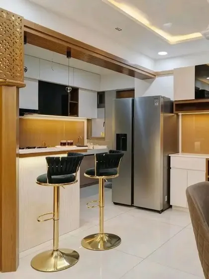 This image shows an open-concept layout where the dining area flows into the kitchen, connected by a stylish breakfast counter. The gold-accented bar stools add a touch of glamour to the space.