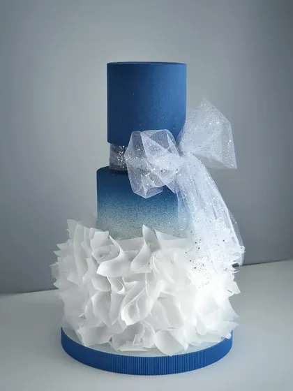 This dreamy three-tiered blue cake features a dramatic glitter fade, wafer paper ruffles, and a sparkling tulle bow. Learn how to combine different textures and materials for a truly unique design.