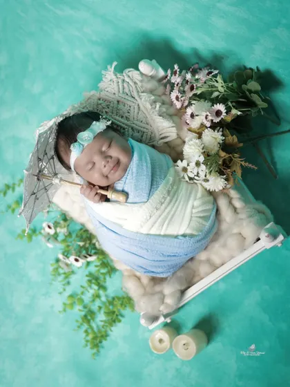 A happy, smiling newborn holds a tiny umbrella prop. Capturing these joyful, sleepy smiles is one of the highlights of our newborn sessions.