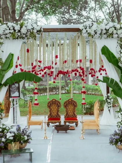 A classic South Indian ceremony setup with elegant gold chairs, banana leaf accents, and hanging floral strings of jasmine and roses.