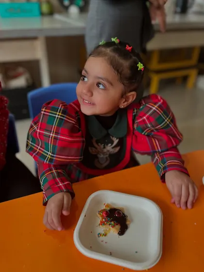 A young girl smiles with delight at her decorated cookie during our Christmas workshop. Holiday-themed activities make learning festive and fun.
