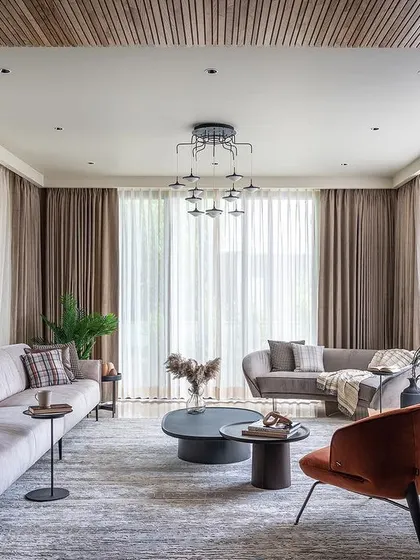 This living room demonstrates a clean, contemporary aesthetic with a touch of warmth. I balanced the neutral tones of the sofas and drapes with a pop of burnt orange in the armchair and a slatted wood ceiling, creating a sophisticated yet inviting residential space.