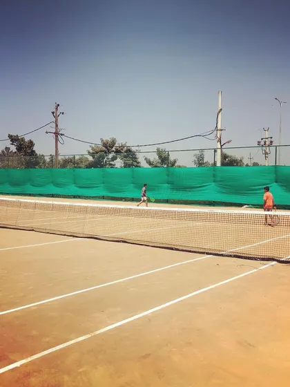 Two players warming up on the clay courts, viewed from behind the net at the Tennis360 Academy.