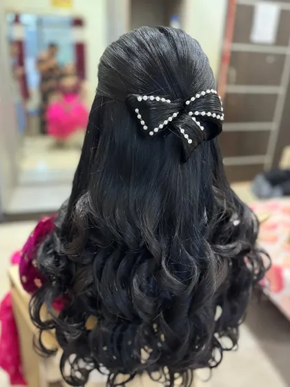 A half-up style with soft curls, featuring a prominent hair bow made of black pearls. This is a modern and chic accessory choice that makes the hairstyle stand out.