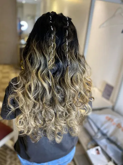 A modern hairstyle with ombre-colored hair, styled in loose curls with sparkling chains woven through the top sections.