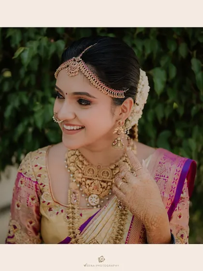 A classic South Indian bridal look featuring a neat bun adorned with jasmine flowers and a traditional matha patti. This is a timeless and elegant choice for the main ceremony.