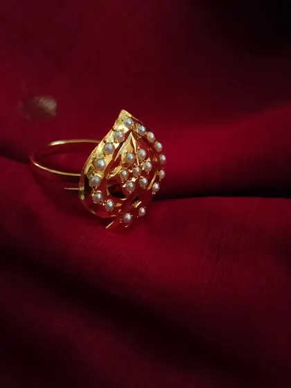 The "Parn" adjustable ring is designed with a unique, leaf-like shape and studded with pearls. This image captures its delicate and artistic form on a rich, red silk background.