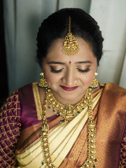 A close-up of Dr. Shakthi's serene muhoortham look. The focus here is on the eyes, with a soft gold and brown eyeshadow blend and winged liner, paired with a deep red lip and traditional temple jewelry.