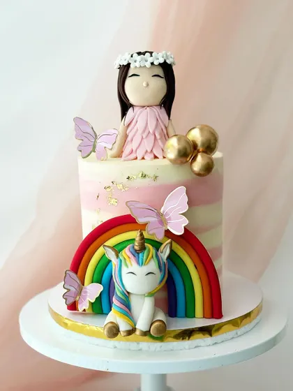This cake combines a unicorn, a rainbow, and a fairy-like figure for the ultimate magical birthday. The striped pink and white buttercream adds another layer of detail.