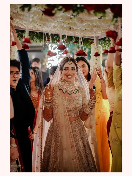 The bride's joyful entrance. Her radiant smile is the centerpiece of this photo as she walks under a canopy of flowers, surrounded by her happy family and friends.