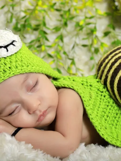 I love getting creative with unique themes. This adorable shot features a baby in a hand-knitted snail costume, sleeping peacefully on a soft blanket against a leafy green background.