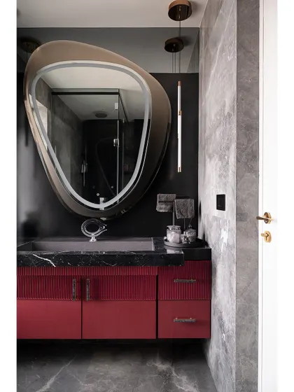 This view of the master bathroom highlights the interplay of color and texture. The deep red of the vanity, the dark grey of the walls, and the organic shape of the mirror create a space with a distinct and powerful character.
