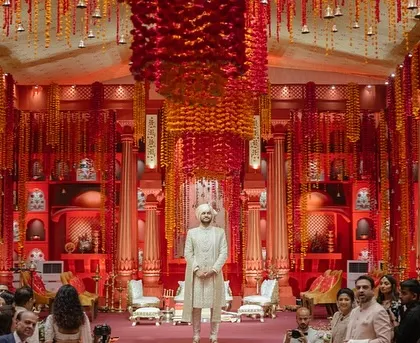 The groom's entrance at the Lal Bagh wedding. The grand scale of the custom-built temple structure, with its towering red pillars and cascading flowers, creates a powerful and unforgettable moment.