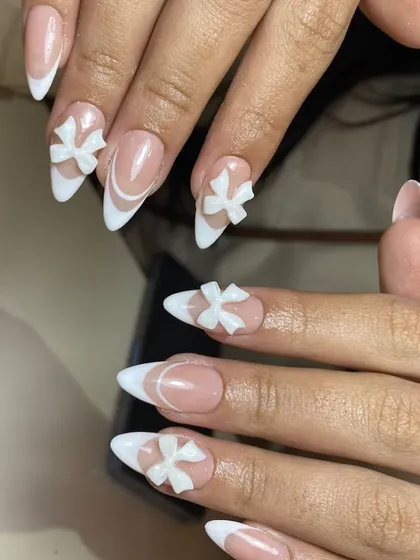 All about the bows. This sharp, stiletto-shaped French manicure is adorned with perfectly sculpted 3D white bows for a cute and coquette vibe.