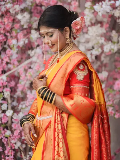 A beautiful portrait of a bride in a yellow and red saree, set against a soft pink floral background. The colors complement each other perfectly.