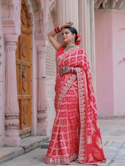 A wide shot showing the woman standing before a large wooden door. The contrast between the pink walls and the red saree creates a visually stunning image.