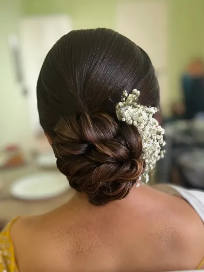 A simple and elegant low bun with a touch of baby's breath, a versatile look for any wedding event.
