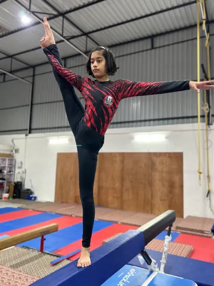 A young gymnast holds a beautiful scale on a low beam, demonstrating excellent balance and flexibility.