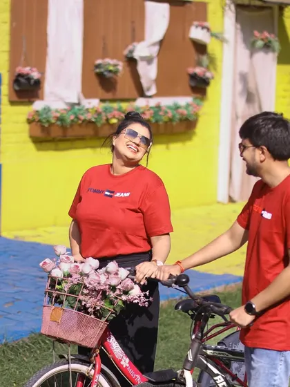 A joyful and bright pre-wedding photograph. The couple shares a laugh with a bicycle adorned with flowers, creating a cheerful and charming scene.