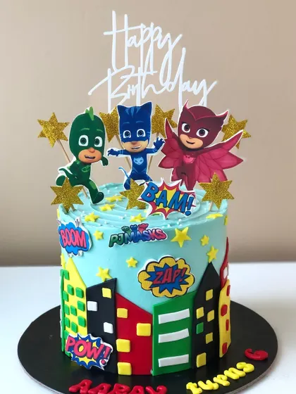 Into the night to save the day! A PJ Masks cake featuring Catboy, Owlette, and Gekko against a city skyline.