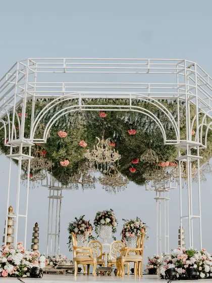 A closer look at the mandap's canopy, which is a dense ceiling of greenery and pink flowers, with dozens of small chandeliers hanging down to create a magical, twinkling effect.