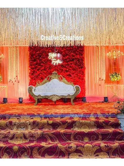 A classic reception stage with a red floral wall and elegant white sofa. The warm lighting and traditional patterned carpet create a timeless and regal look.