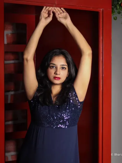 This studio portrait uses a simple but effective pose with arms raised, framed by the bold red background for a striking composition.