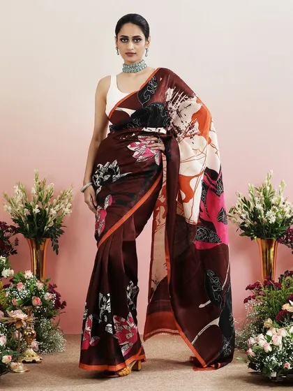A brown saree with a bold, abstract floral print in shades of orange, pink, and black.