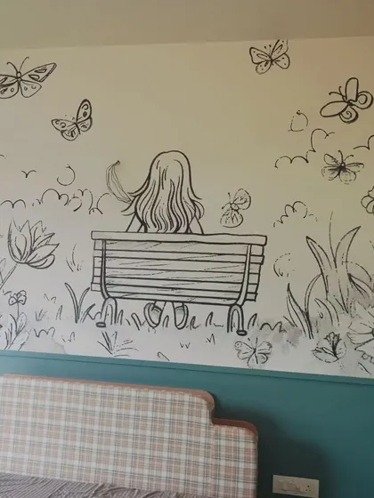 A simple and charming line-art mural of a girl on a bench surrounded by butterflies. This is a great choice for a subtle yet personal touch in a bedroom.