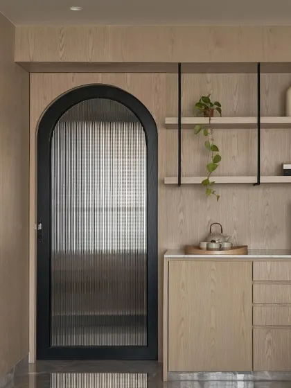 An arched doorway with a fluted glass panel provides a beautiful transition point within the master suite, separating the coffee bar area from the main bedroom while allowing light to flow between the spaces.