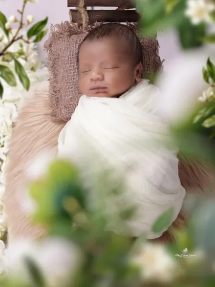 A close-up, artistic shot of a swaddled newborn. We use creative framing with foreground flowers to add depth and a dreamy quality to the photograph.