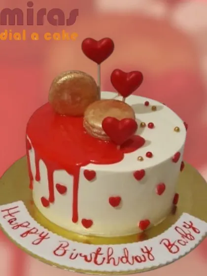 A romantic heart-themed cake with a red drip and macaron toppers. The combination of red hearts and golden macarons creates a look that is both loving and luxurious.