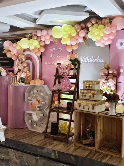 A wide view of a fairy-themed birthday party, showing the full arrangement of props, including rustic crates, decorative shelves, and a large marquee number.