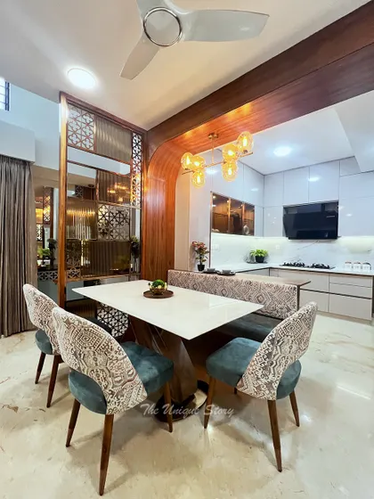 The dining area features a combination of upholstered chairs and bench seating for flexibility. A stunning amber-toned chandelier hangs above the table, creating a warm focal point that is visible from the adjoining living space.
